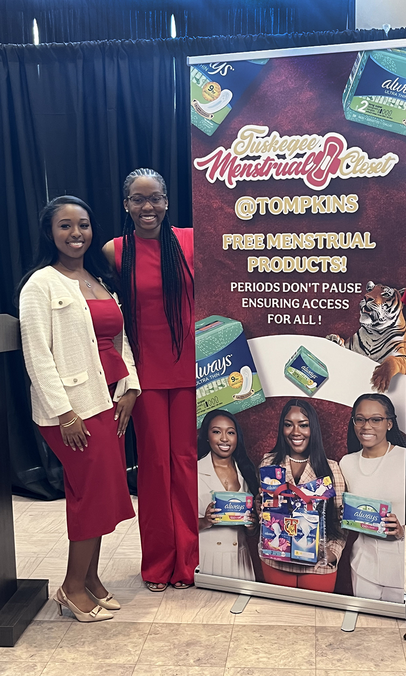 Two female students standing by sign announcing the Comfort Closet