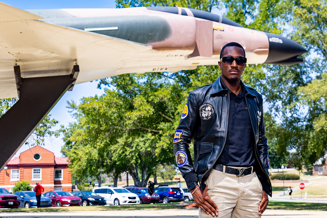 A male student aviator stands in bomber jacket by the Gen. Daniel Chappie James airplane
