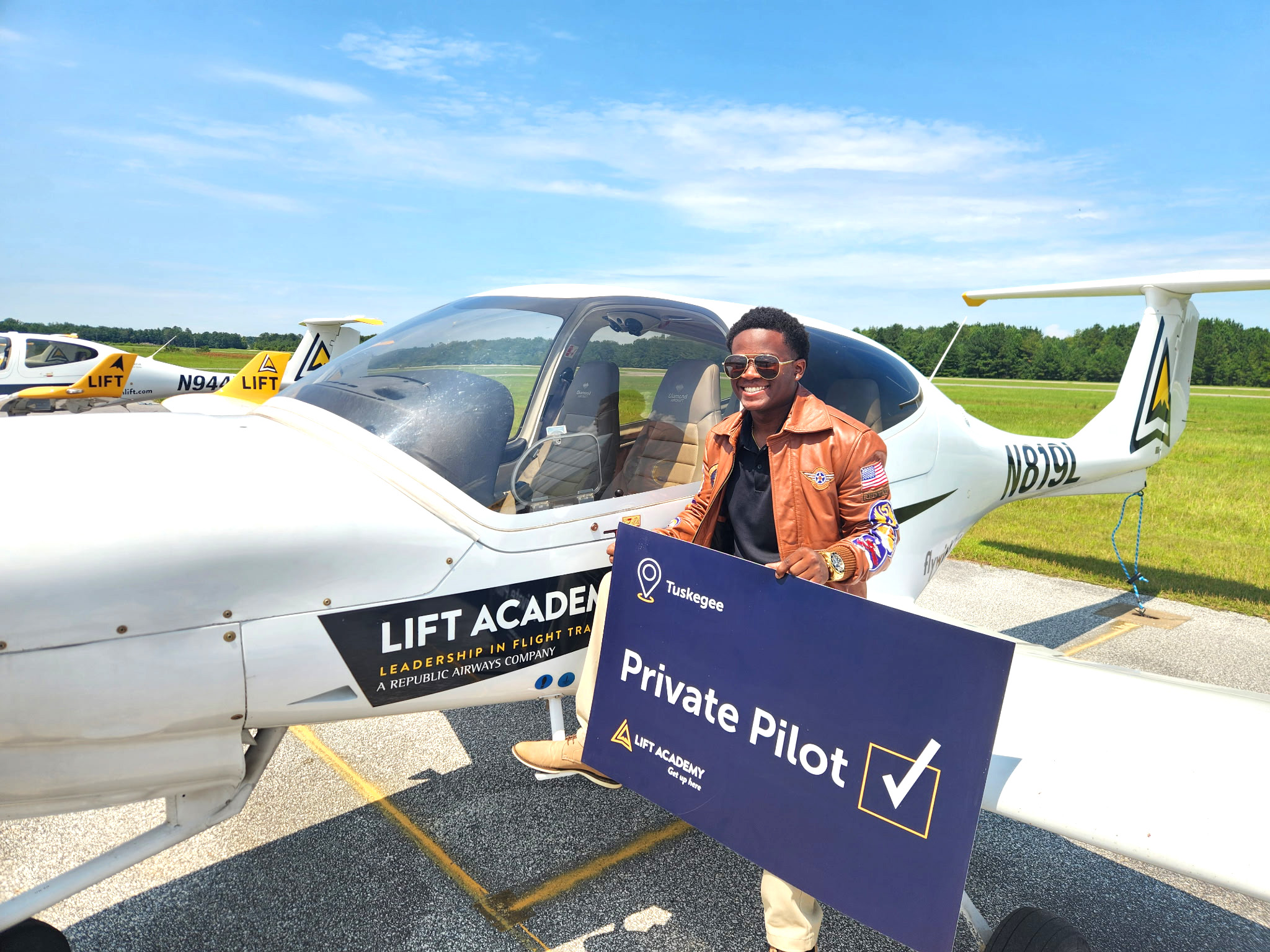 Picture of Isaiah Hand standing at airplane holding a sign.