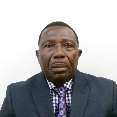 Head-and-shoulders portrait of a man wearing a dark suit jacket, checkered shirt, and patterned tie against a white background.