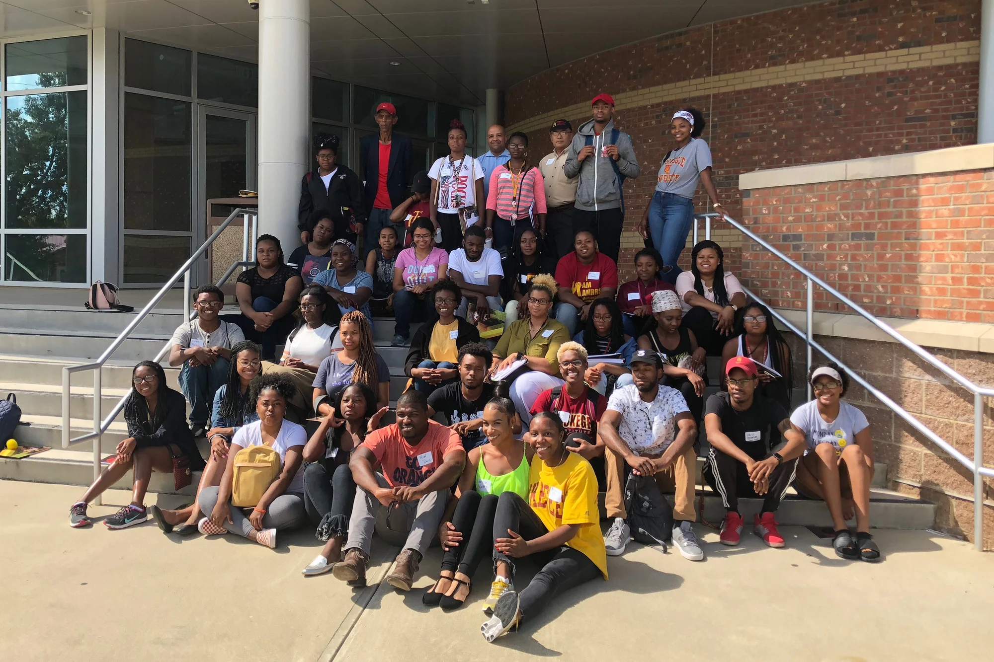 Large group of students and adults posing on outdoor steps outside a brick building entrance.