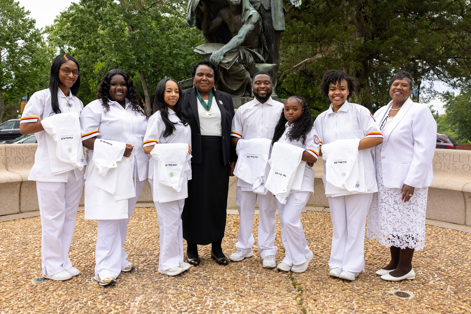School of Nursing and Allied Health graduating students holding their white coats standing at the monument with their Dean