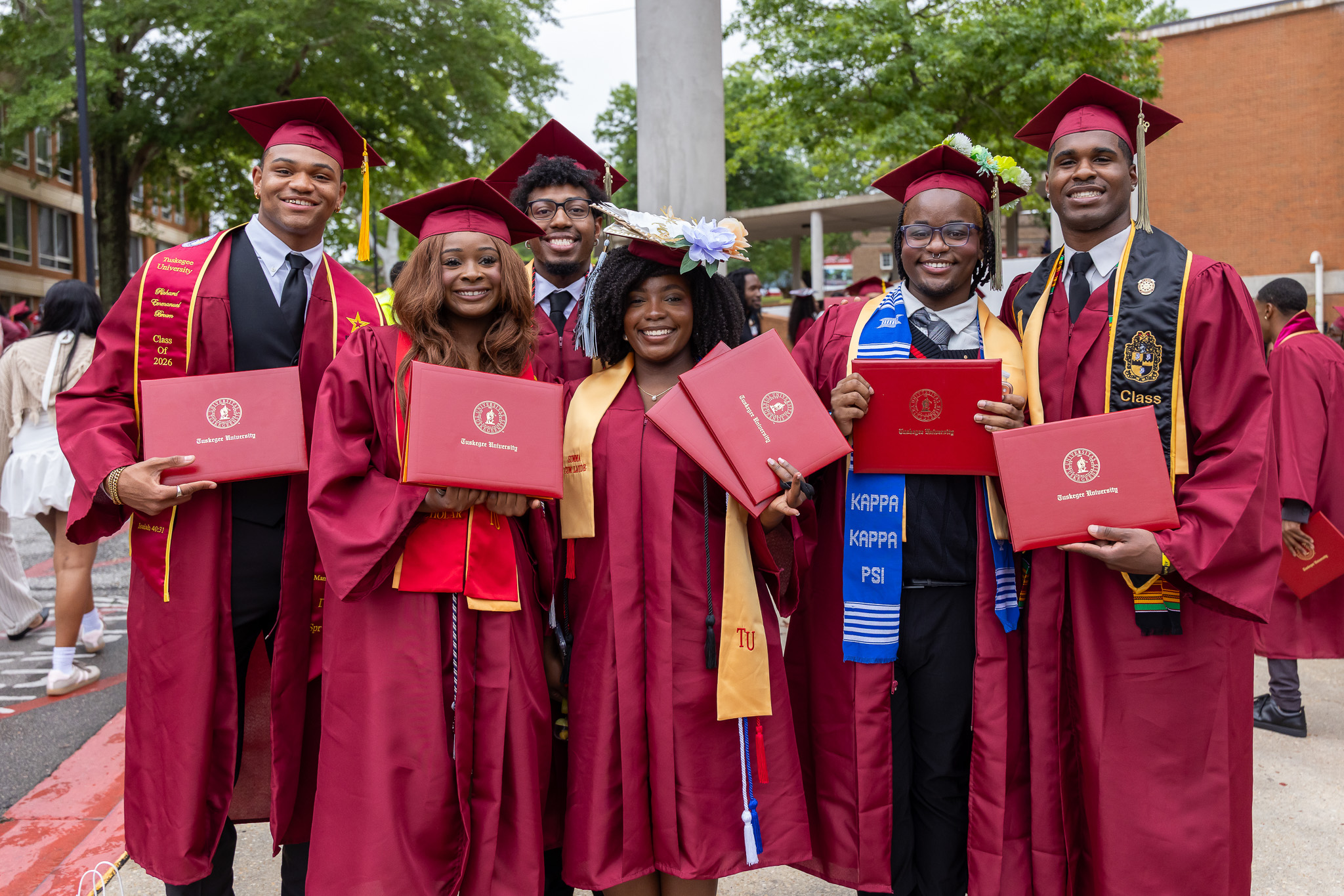 Graduates in cap and gowns standing outside holding diplomas