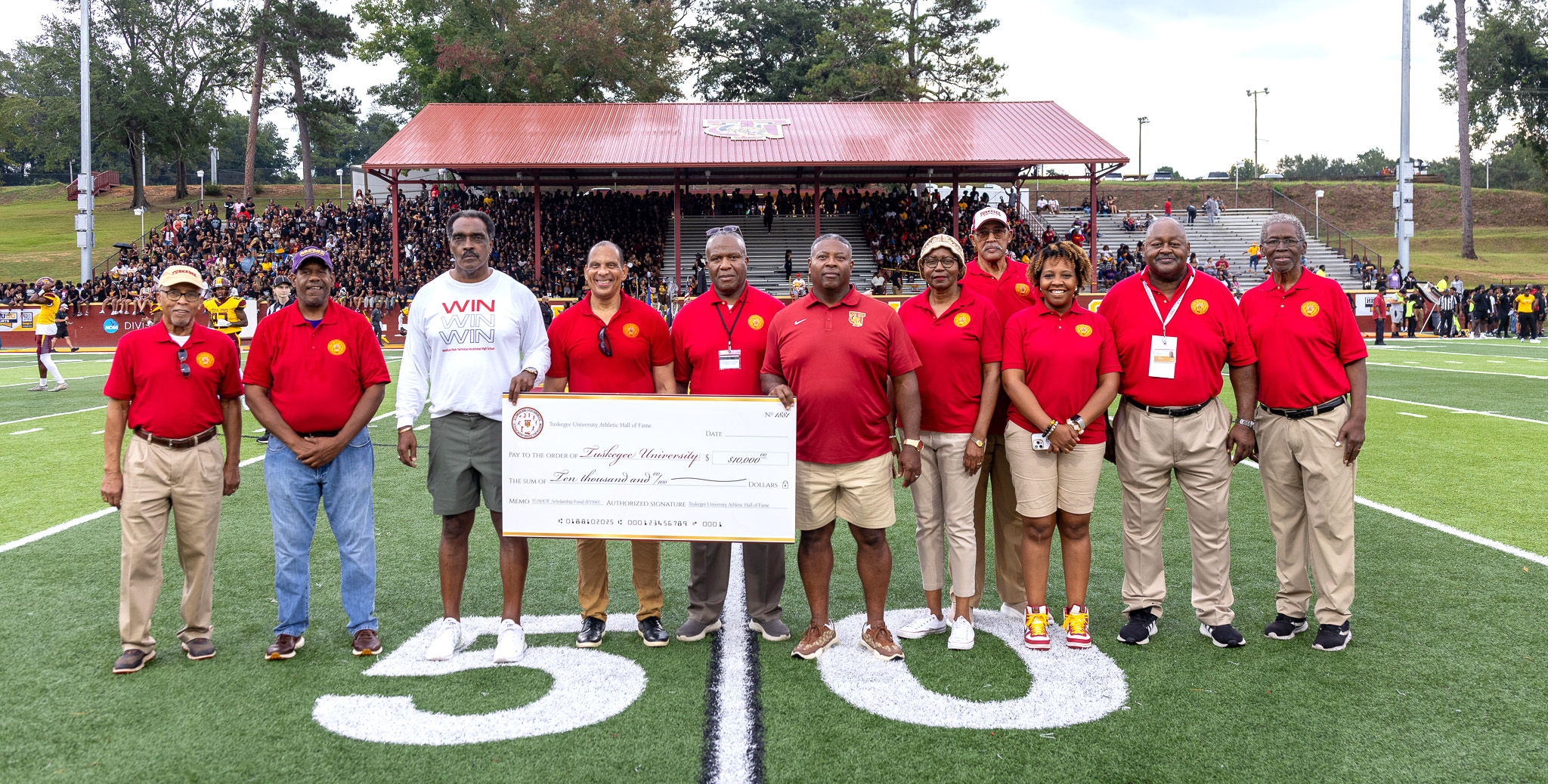Picture of 11 Hall of Fame inductees standing on the field holding a check