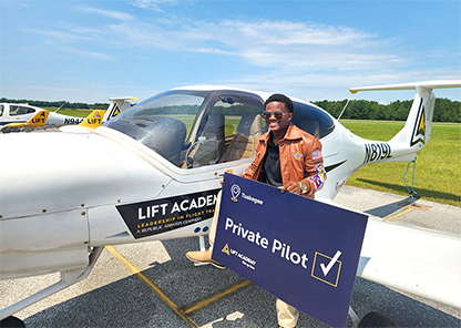 Picture of Isaiah Hand standing at airplane holding a sign.